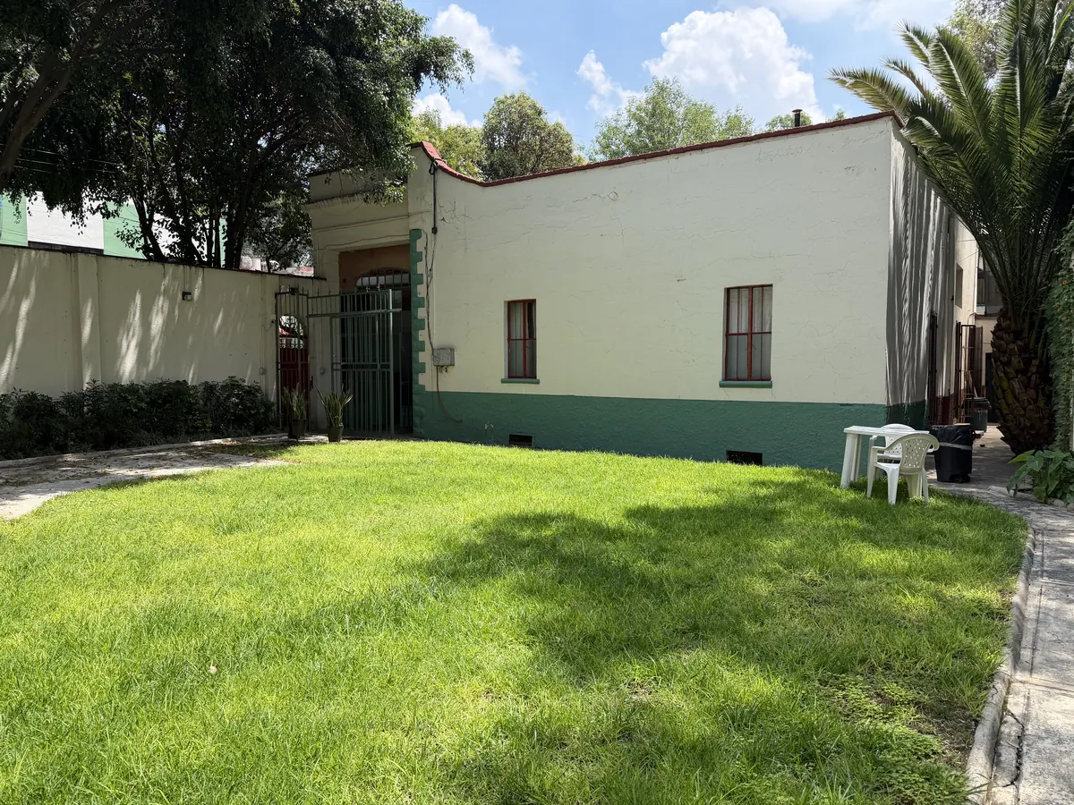 Jardín arbolado de Casa Popotla con césped y fachada blanca